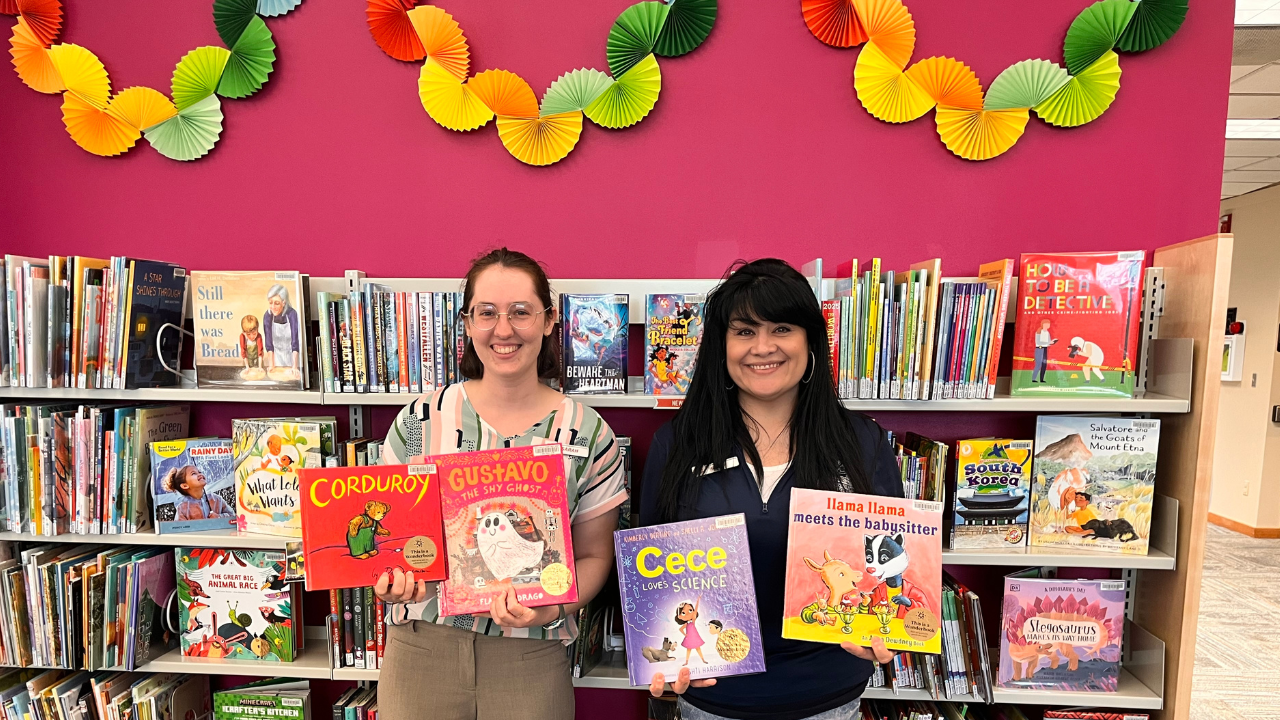 two staff members holding up four wonderbooks to checkout