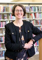 Sarah in black jacket leaning on bookshelf