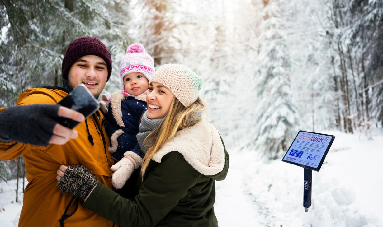 happy family walking in the park taking a selfie in front of the StoryWalk sign