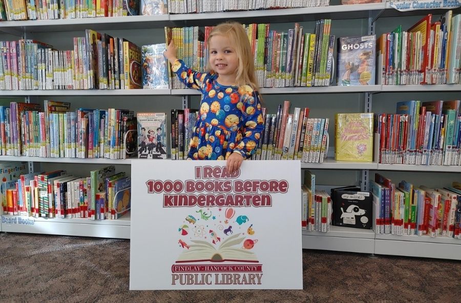 child holding a yard sign that says I read 1000 books before kindergarten