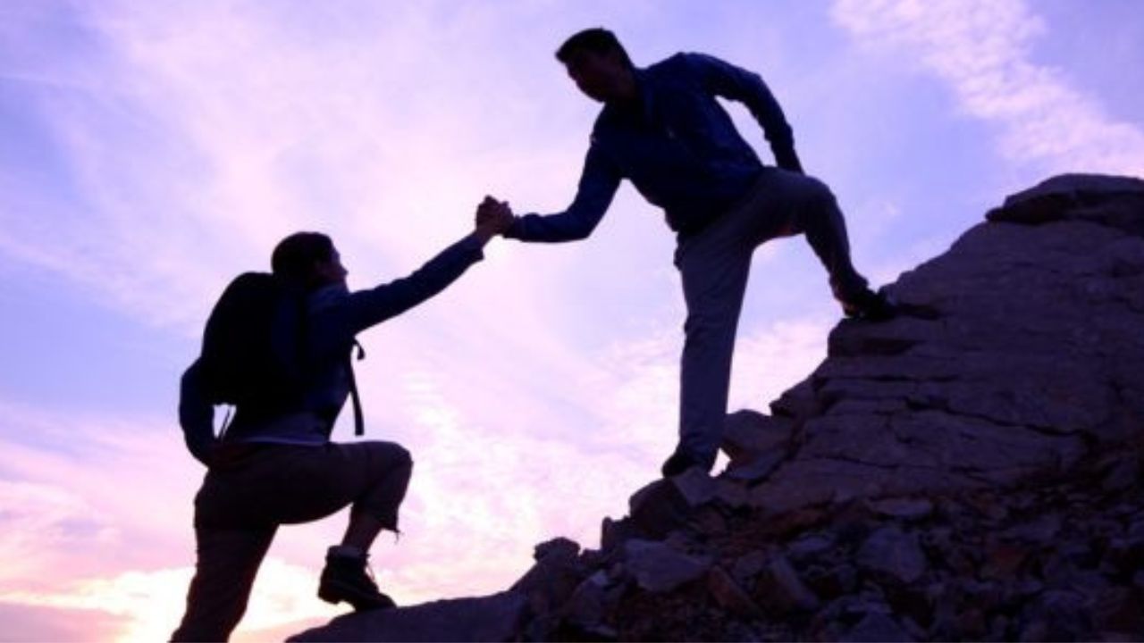 man helping a woman up a mountain