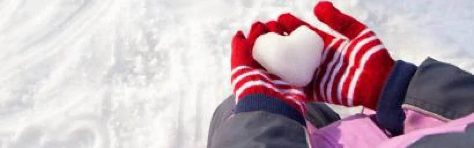 mittens on hands with heart made of snow 